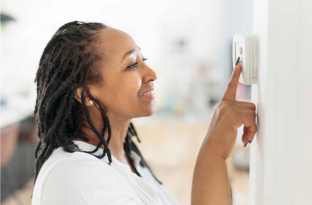 A woman adjusting the thermostat on the wall of her home