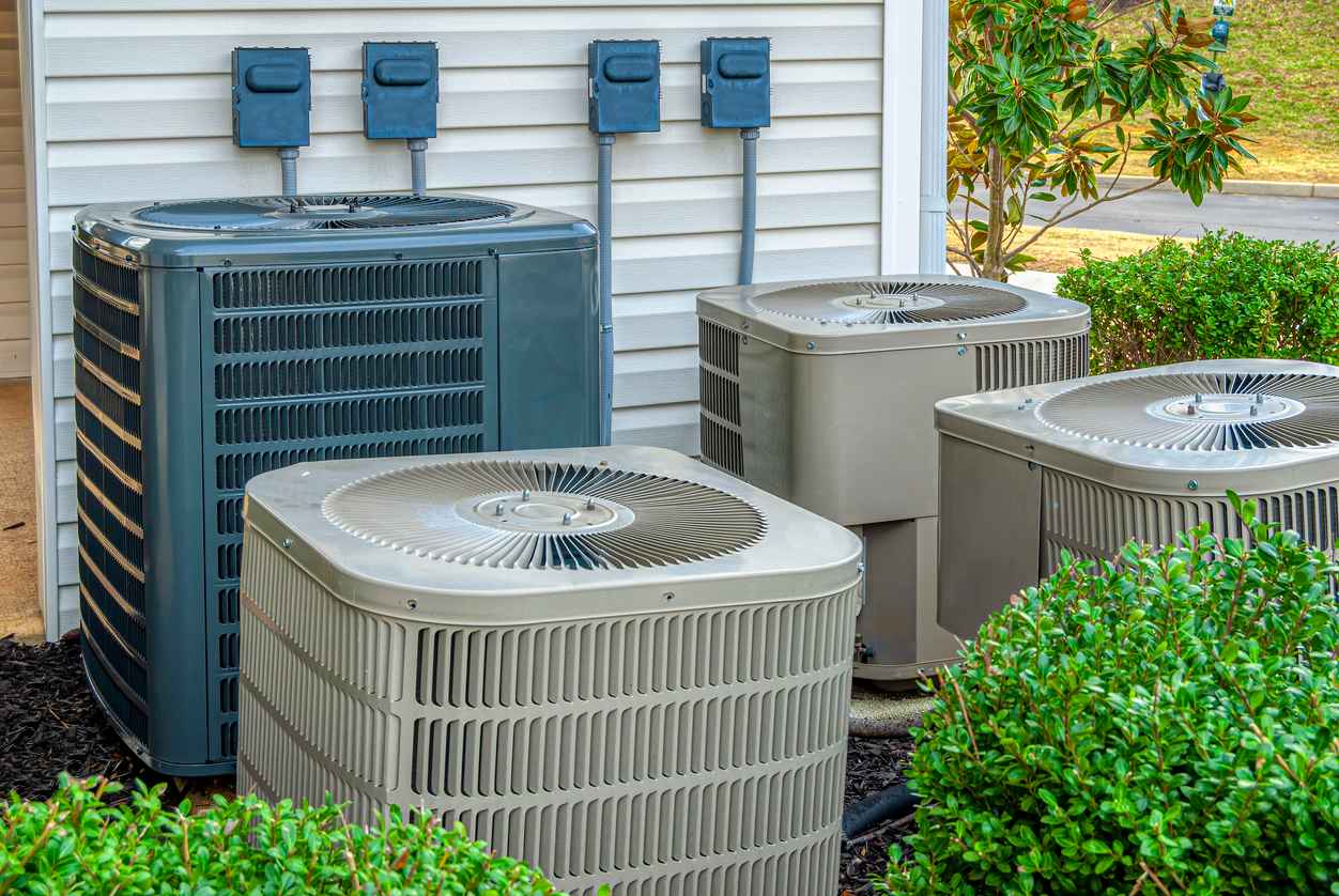 Horizontal shot of four air conditioning units outside a residential complex.